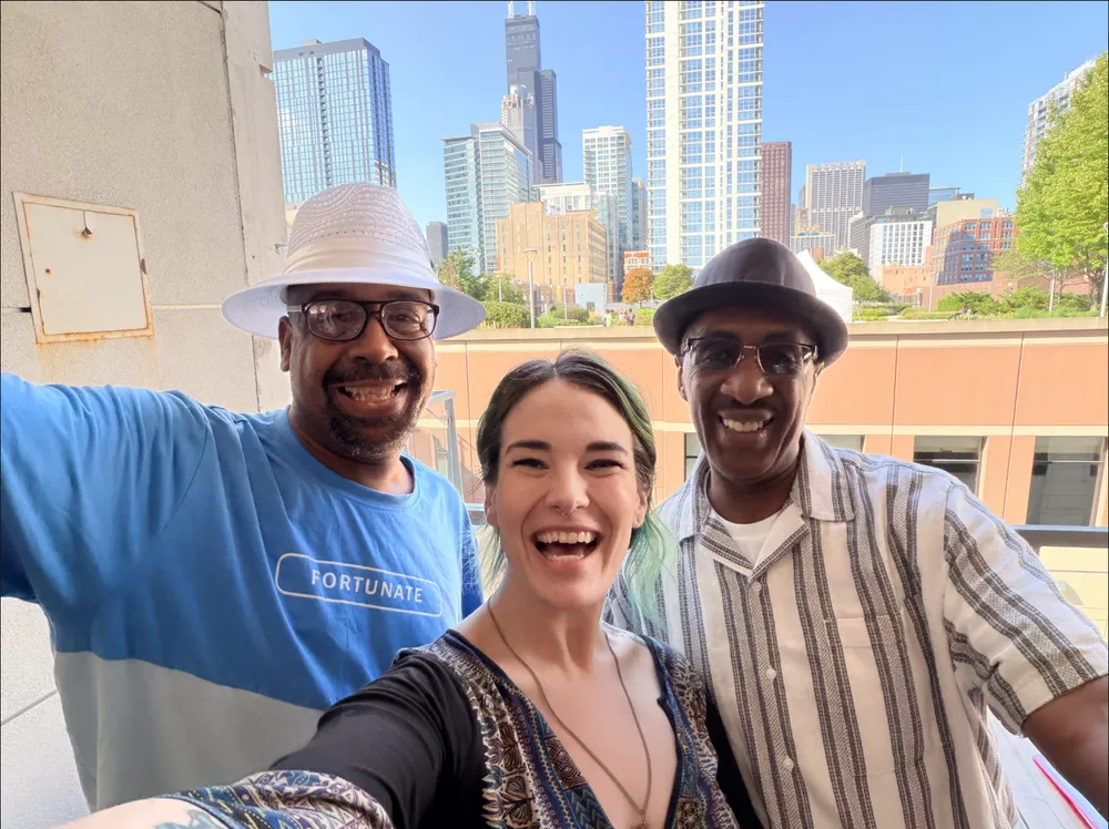 Leigh with Michael and Greg of Company 773, smiling together on a sunny terrace with the Chicago skyline behind them